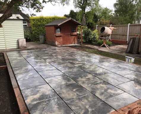 Concrete slab foundation in a garden, with a shed and other structures in the background.