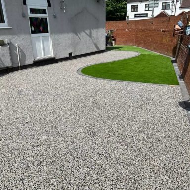 Gravel driveway with a curved edge, leading to a small green lawn area.