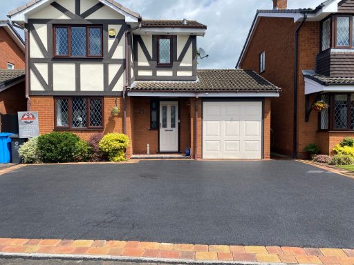 A two-storey house with a garage, surrounded by a garden and a paved driveway.