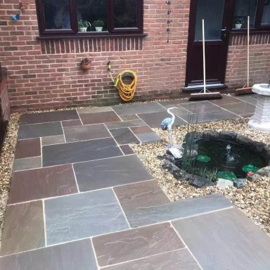 Paved outdoor area with stones and a small pond, surrounded by gravel and tools.