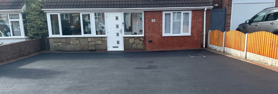 A tidy driveway in front of a brick house with white door and wooden fence.