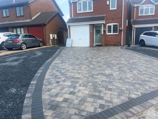Paved driveway leading to residential homes, featuring grey and brown block paving.