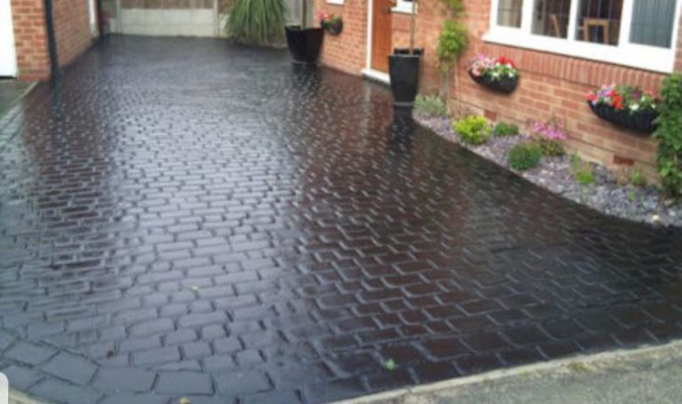 Patterned black paving with flower beds, in a residential setting.
