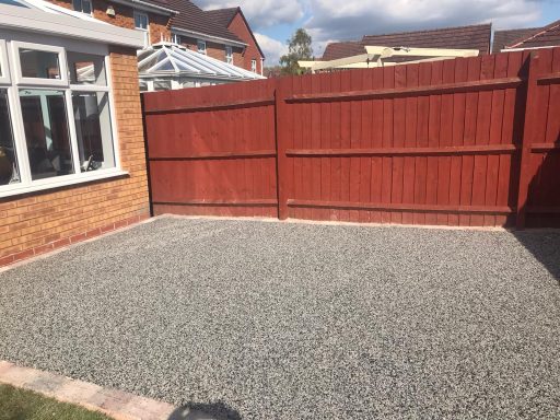 Gravelled area enclosed by wooden fence, with a house visible in the background.