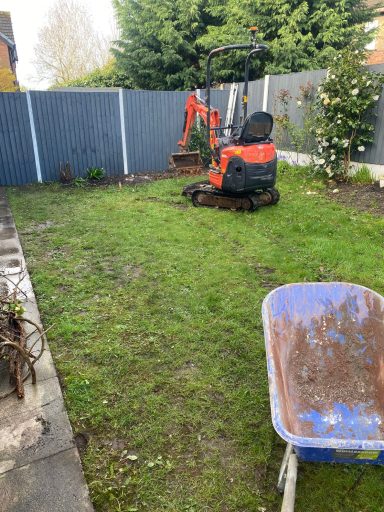 Small garden with a red digger and a wheelbarrow, surrounded by hedges and plants.