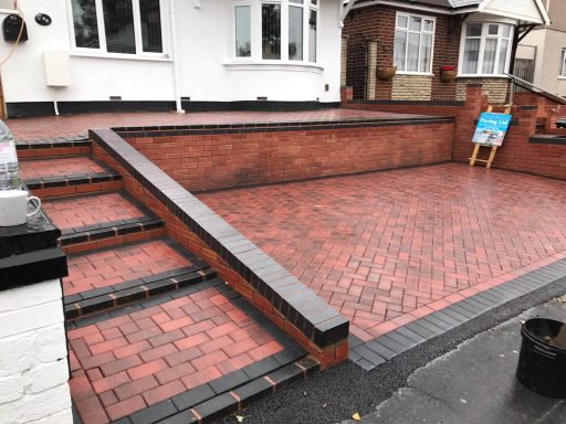 Red brick paved driveway with steps leading up to a house.