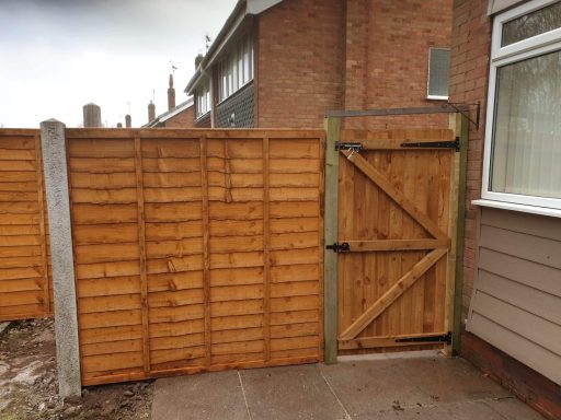 Wooden garden gate next to a fence, leading to a pathway by a house.