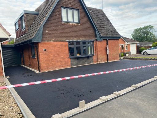 A freshly paved black asphalt driveway in front of a brick house.