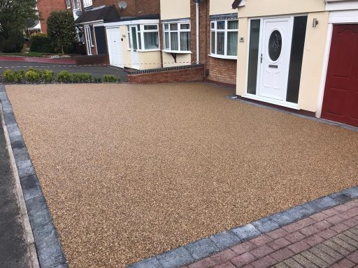A stone driveway with a smooth, beige surface beside a brick pathway and house.