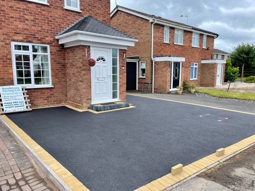 Freshly paved driveway in front of a brick house with a porch.