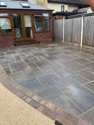 Patio area with stone slabs, leading to a wooden door and surrounded by a fence.