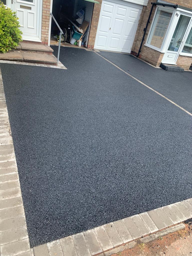 Newly resurfaced black asphalt driveway with adjacent brick edging.