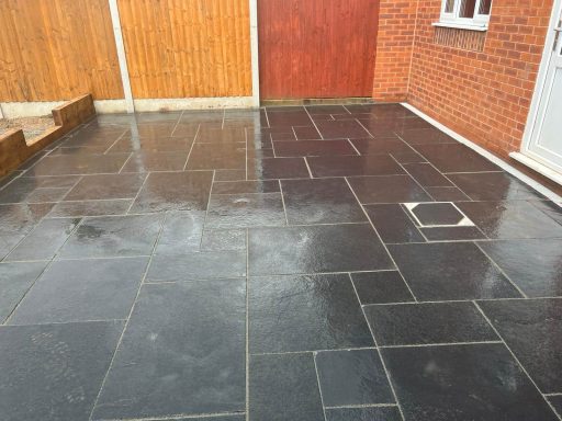 Wet patio area with grey stone paving and wooden fence in the background.