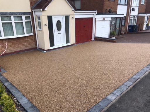 A gravel driveway beside a house, with a red garage door and paved border.