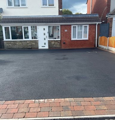 Bungalow with a red brick façade and a paved drive under a partly cloudy sky.