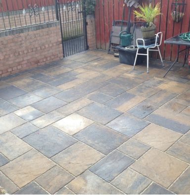 Paved patio area with grey and beige stone tiles, surrounded by a fence and planters.