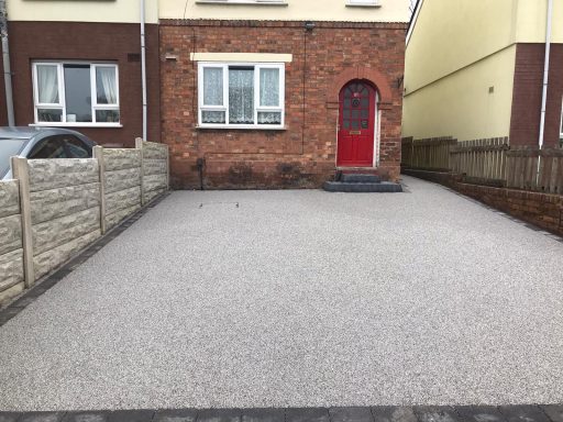 Front view of a house with a red door and gravel driveway, bordered by fences.