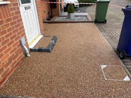 Pathway leading to a front door with a gravel surface and green and blue bins nearby.