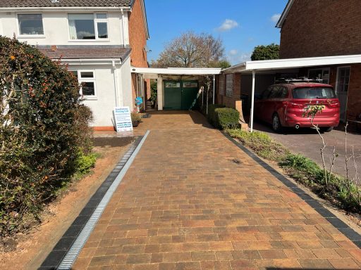 Paved driveway leading to a garage and house, with green hedges and blue sky.