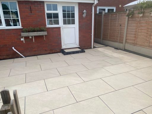 Paved patio area with a door, adjoining a brick wall and fenced garden.