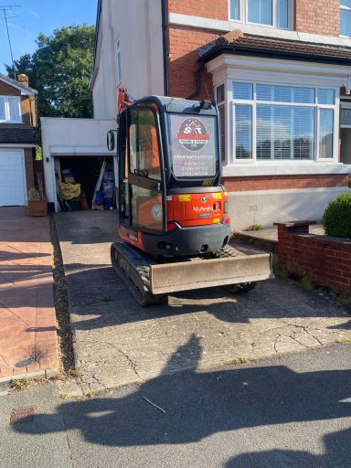 Small excavator parked on a driveway beside a house.