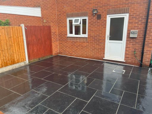 Paved outdoor area next to a brick house, wet from recent rain.