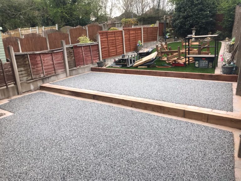 Gravel patio and landscaped garden area with wooden borders and green plants.