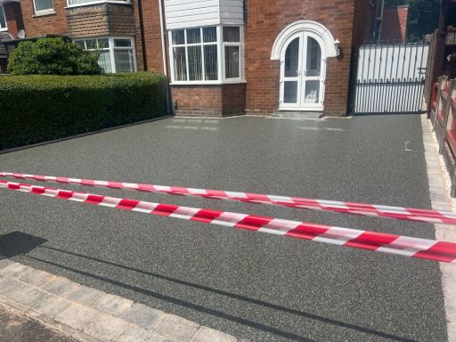 Freshly laid grey tarmac driveway with white house and red and white barrier tape.