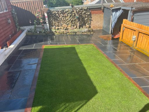 Lawn and patio area with sunlight and a shadow from a nearby wall.