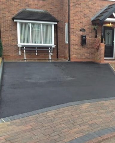 A smooth, black driveway leading to a brick house with a front porch.