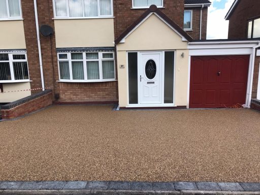 Front exterior of a house featuring a white door, gravel driveway, and red garage door.