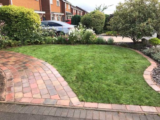 Well-maintained garden with a lawn, brick pathway, and various plants.