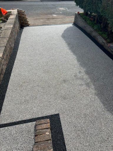 Driveway made of grey gravel with black edging and lined with shrubs.
