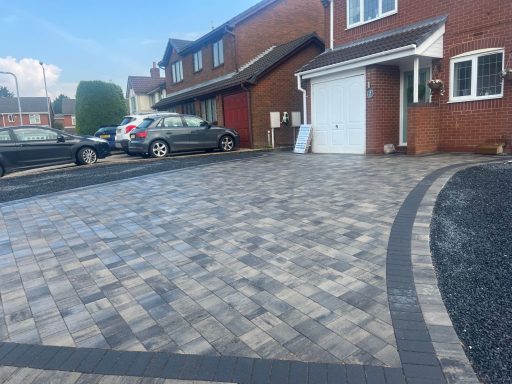 A freshly paved driveway with grey block paving and parked cars in a residential area.