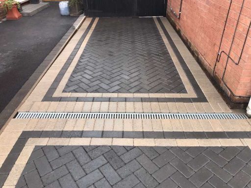 Patterned paved driveway with contrasting tiles in a herringbone design.