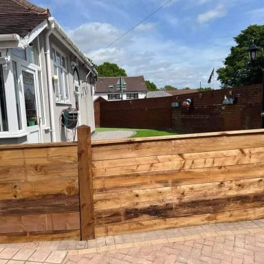 Wooden fence in front of a house with a green lawn and blue sky in the background.