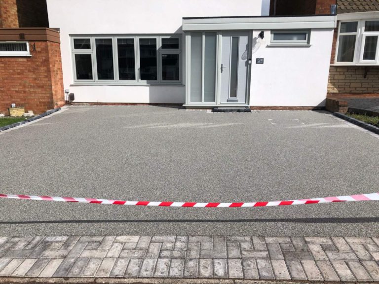 A gravel driveway in front of a modern house, cordoned off with barrier tape.