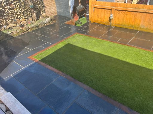 Patio area with slate tiles and a patch of green grass.