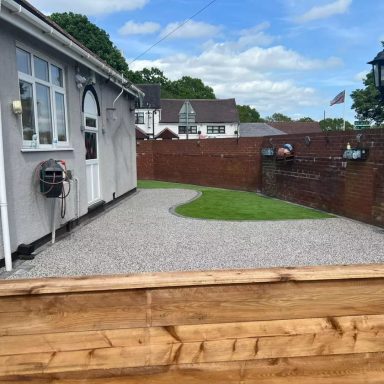 Garden path with gravel and grass, surrounded by a wooden fence and houses in the background.