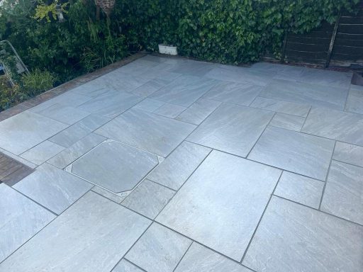 Paved patio area with grey stone tiles surrounded by greenery.