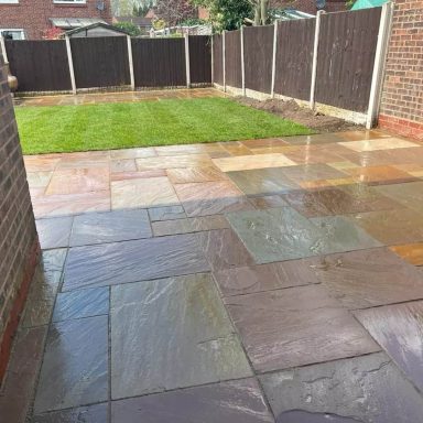 Stone patio with a well-maintained grass lawn and wooden fencing in the background.