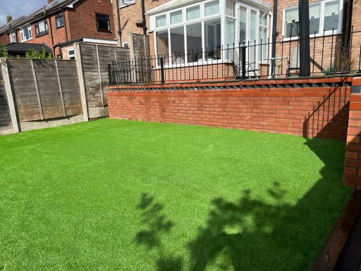 Lush green artificial grass in a garden with brick walls and a residential backdrop.