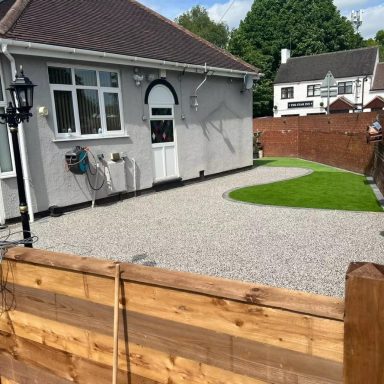 Bungalow with a gravel garden and lawn, bordered by wooden fencing.