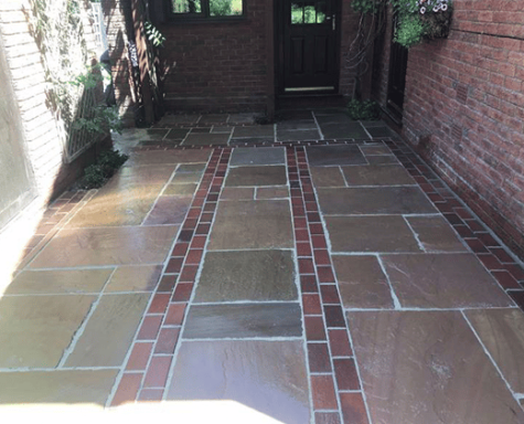 Paved patio with decorative brick borders and wooden door in the background.