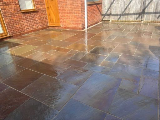 Freshly laid, wet stone patio with varied colour tones and a wooden door in the background.