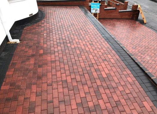 Paved surface with interlocking red and black bricks in a driveway layout.
