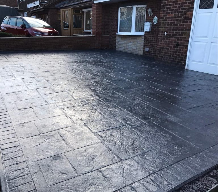 Patterned black driveway with a house and window in the background.