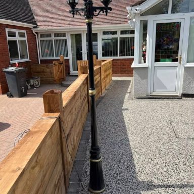 Black streetlamp beside a gravel path and wooden fencing outside a house.