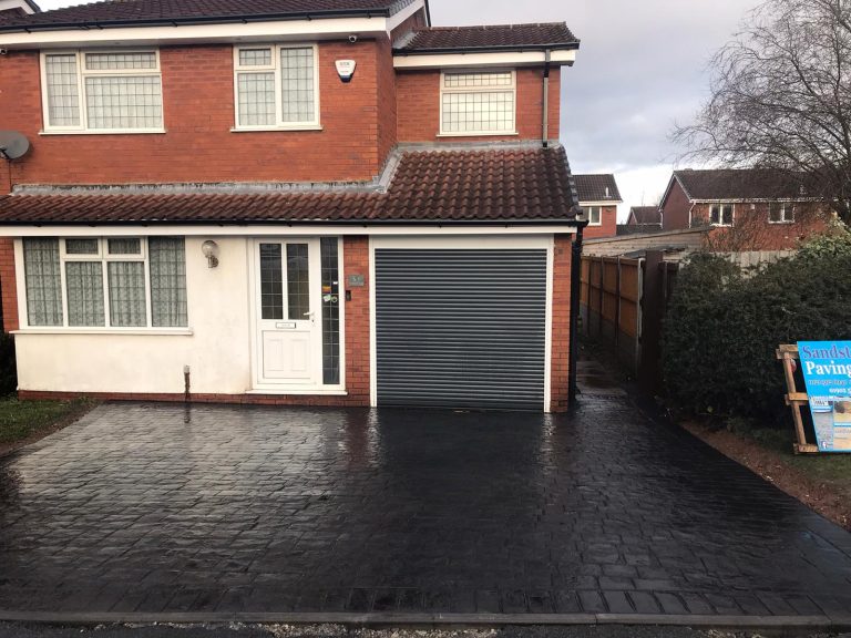 Detached brick house with a grey garage door and a newly paved driveway.