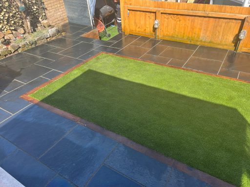 A garden patio with slate tiles and a patch of artificial grass in sunlight.
